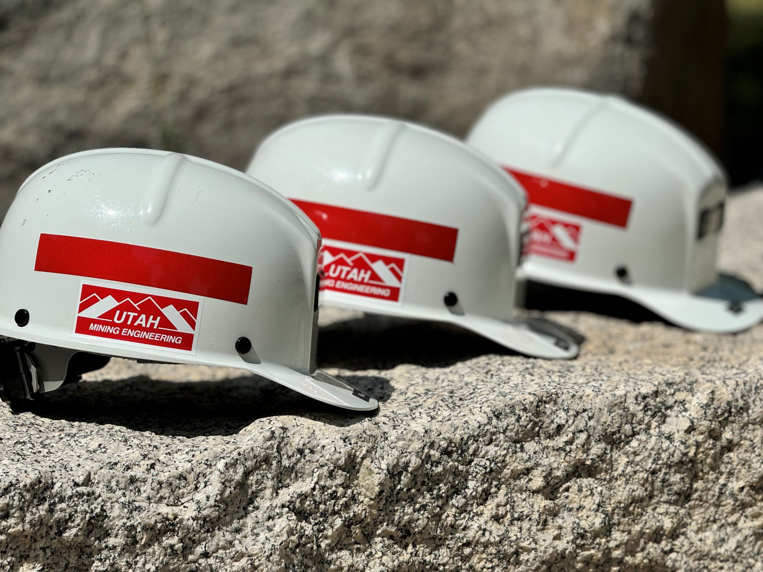 a row of three hard hats with a sticker that reads, 'Utah Mining Engineering'